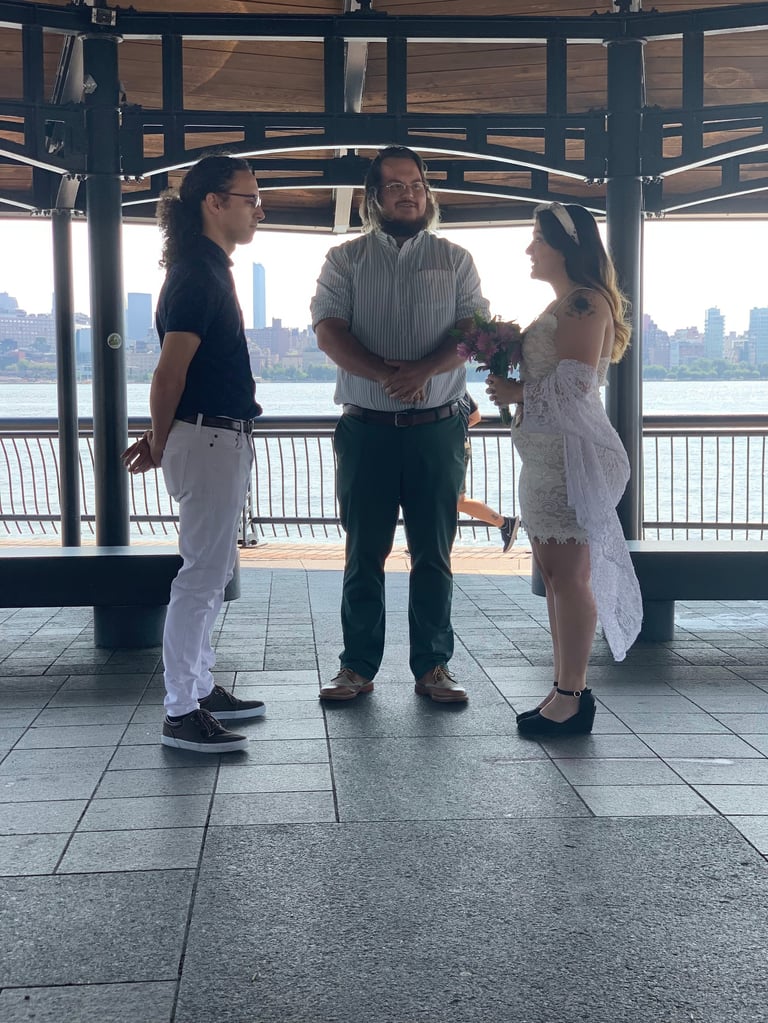 Three people standing in a covered waterfront pavilion with city skyline visible behind them